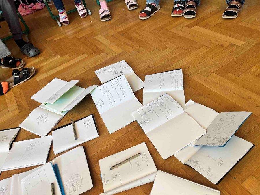 Skizzenbücher liegen am Boden, Kinder im Kreis rundherum